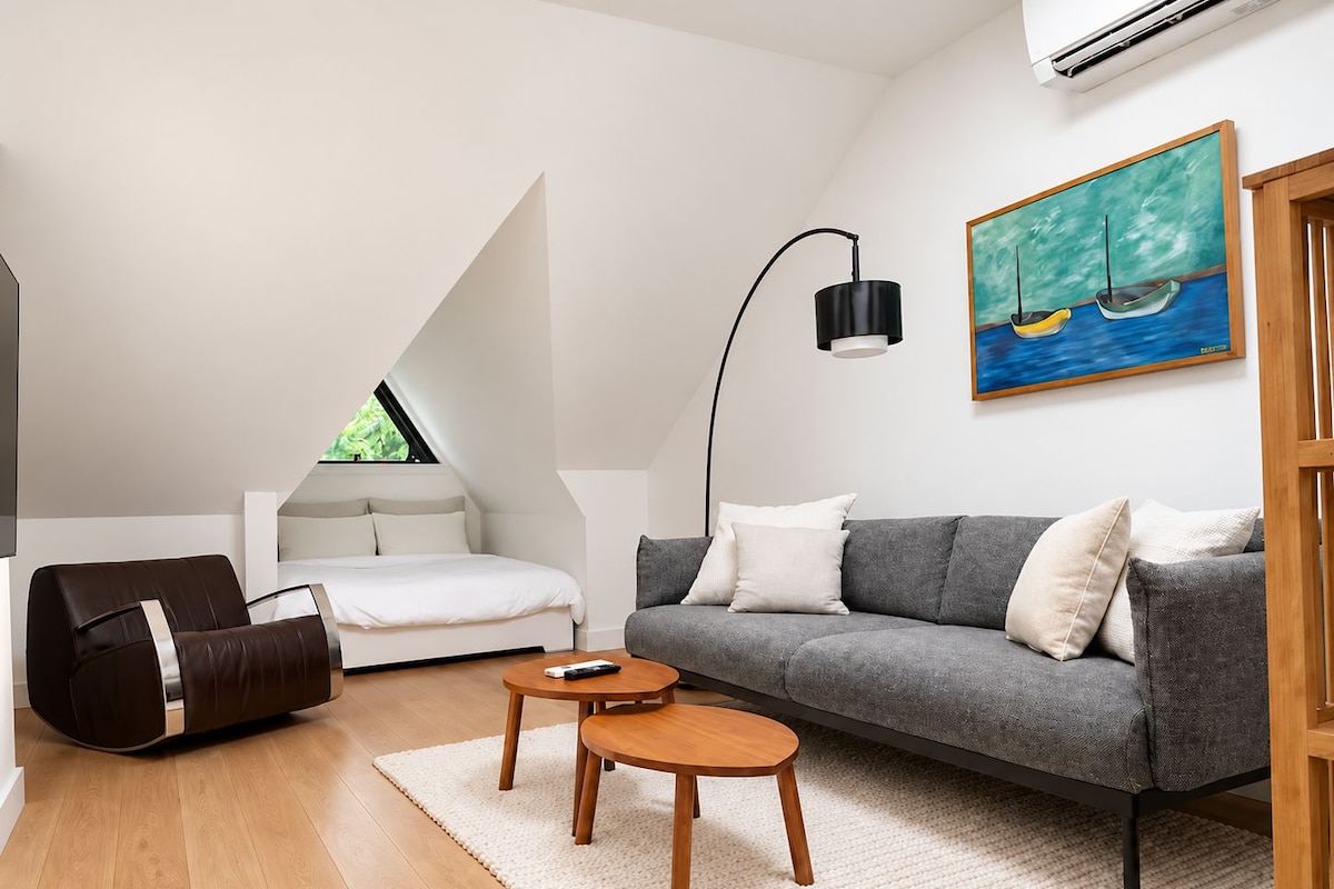 A modern living room with a sofa, a coffee table, a bean bag, and a painting on the wall.