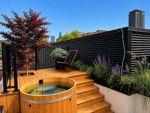 A rooftop garden with a hot tub, wooden steps, a chair, and various plants. - Sumach House (Toronto)