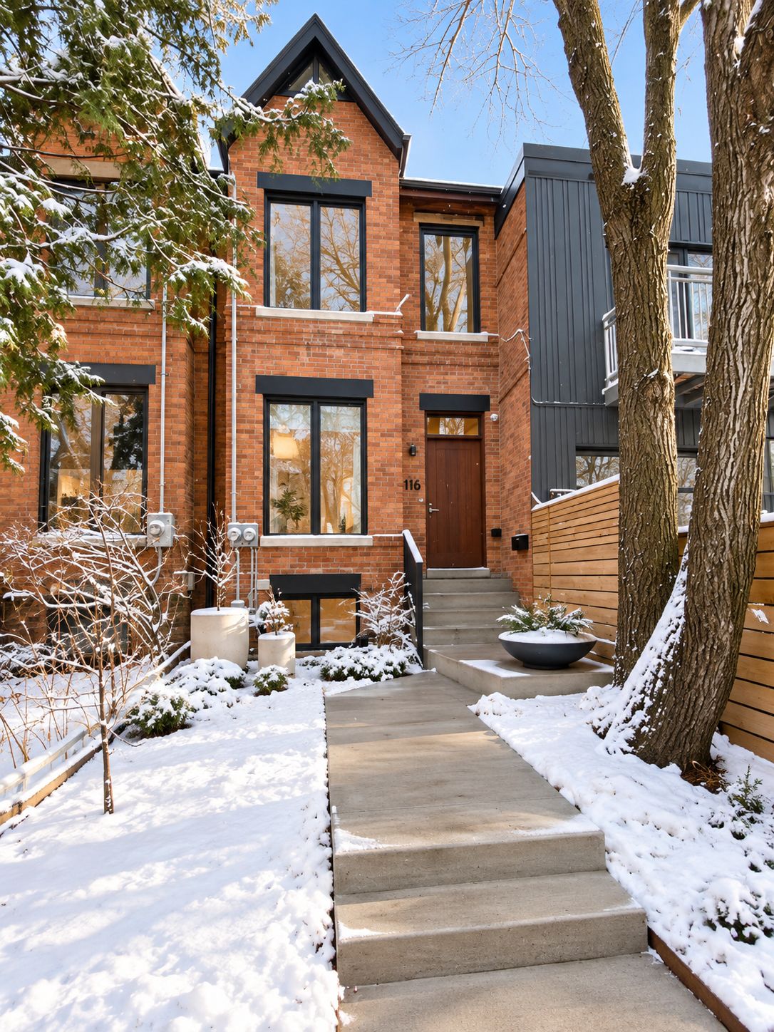 A two-story brick house with a front entrance, a visible number '116', and a snow-covered landscape.