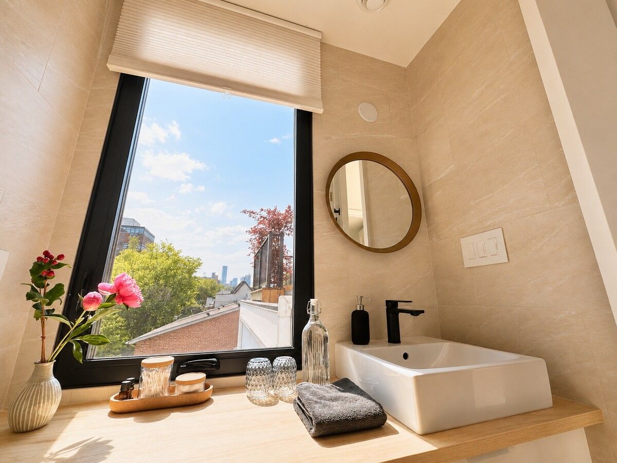 Un baño moderno con un ventanal grande, un espejo redondo y una bañera blanca.