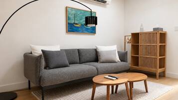 A modern living room with a grey sofa, a wooden coffee table, a painting of a boat, and a black floor lamp.