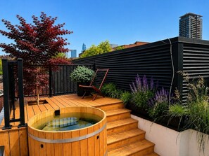 A rooftop garden with a hot tub, wooden steps, a chair, and various plants. - Sumach House (Toronto)