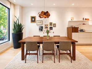 A dining area with a wooden table, six chairs, a vase with flowers, and framed pictures on the wall. - Sumach House (Toronto)