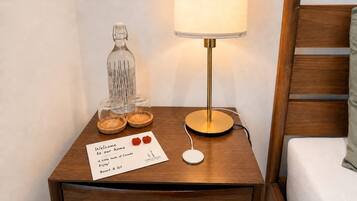 A wooden bedside table with a lamp, a glass bottle, and a welcome card.