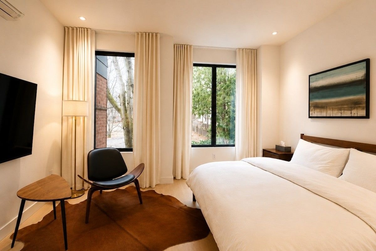 A hotel room with a bed, a chair, a TV, and a window with curtains.