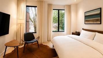 A hotel room with a bed, a chair, a TV, and a window with curtains.