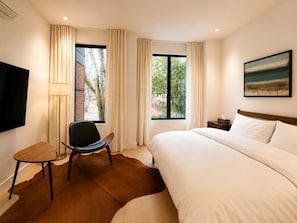 A hotel room with a bed, a chair, a TV, and a window with curtains. - Sumach House (Toronto)