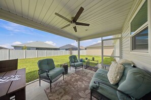 A covered patio area with a ceiling fan, outdoor furniture, and a view of a grassy yard. - Brand-New 3BR · Golf Cart · Fenced Yard · Eastport (Sumterville)