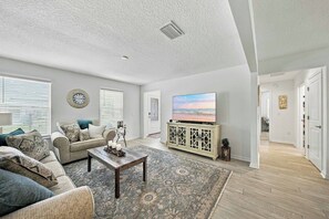 A living room with a sofa, coffee table, and a television on a cabinet. - Brand-New 3BR · Golf Cart · Fenced Yard · Eastport (Sumterville)