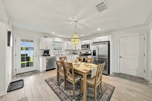 A modern kitchen with white cabinets, stainless steel appliances, and a dining area with a wooden table and chairs. - Brand-New 3BR · Golf Cart · Fenced Yard · Eastport (Sumterville)