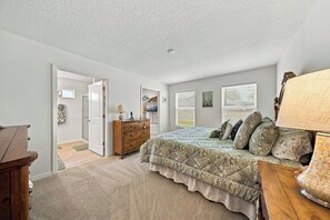 Quarto com cama, penteadeira, abajur e porta que dá para outro cômodo.