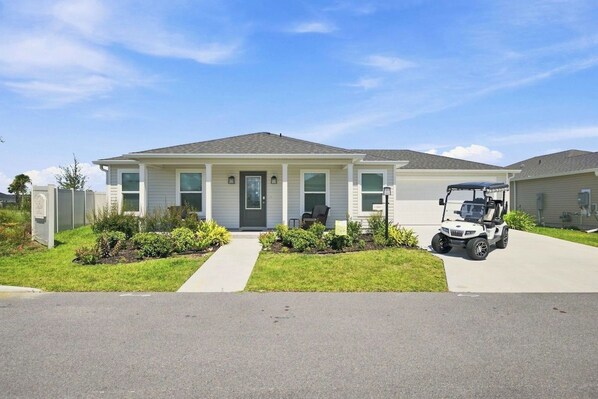 Une maison d’un étage, conçue pour l’habitation, avec un porche à l’avant, une allée et un véhicule de type voiturette de golf garé devant.