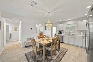 Une cuisine moderne avec des meubles blancs, une table à manger avec des chaises et un lustre.