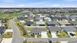 Un quartier résidentiel où les maisons sont alignées en rangées, avec une route sinueuse et un terrain de golf en arrière-plan.