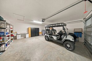 Garagem com carrinho de golfe, prateleiras com materiais de limpeza, uma mesa e uma porta.