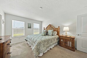 A bedroom with a bed, dresser, nightstand, and two windows with blinds. - Brand-New 3BR · Golf Cart · Fenced Yard · Eastport (Sumterville)