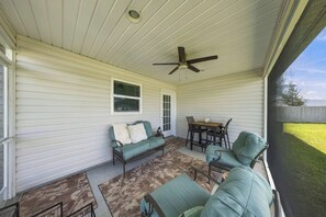 Une véranda couverte avec un ventilateur de plafond, une table à manger avec des chaises et un canapé.