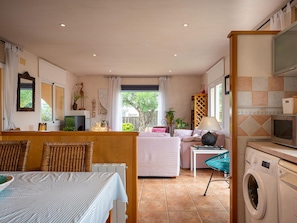 A well-lit room with a bed, a dining table, a washing machine, and a view of the outdoors. - House with garden near the beach - 6 guests (Creixell)