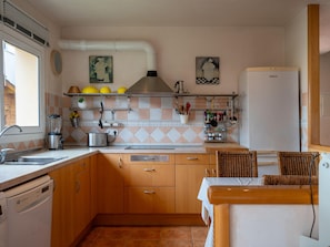 A kitchen with wooden cabinets, a dishwasher, a refrigerator, and a dining area with wicker chairs. - House with garden near the beach - 6 guests (Creixell)