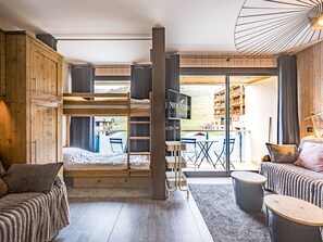 A compact room with bunk beds, a TV, a dining area, and a view of a building outside. - Functional studio, mountain view - 4 guests (La Toussuire)