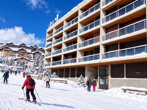 A multi-story building with balconies, a ski slope in the foreground, and snow-covered trees. - Renovated studio, mountain view - 4 guests (La Toussuire)