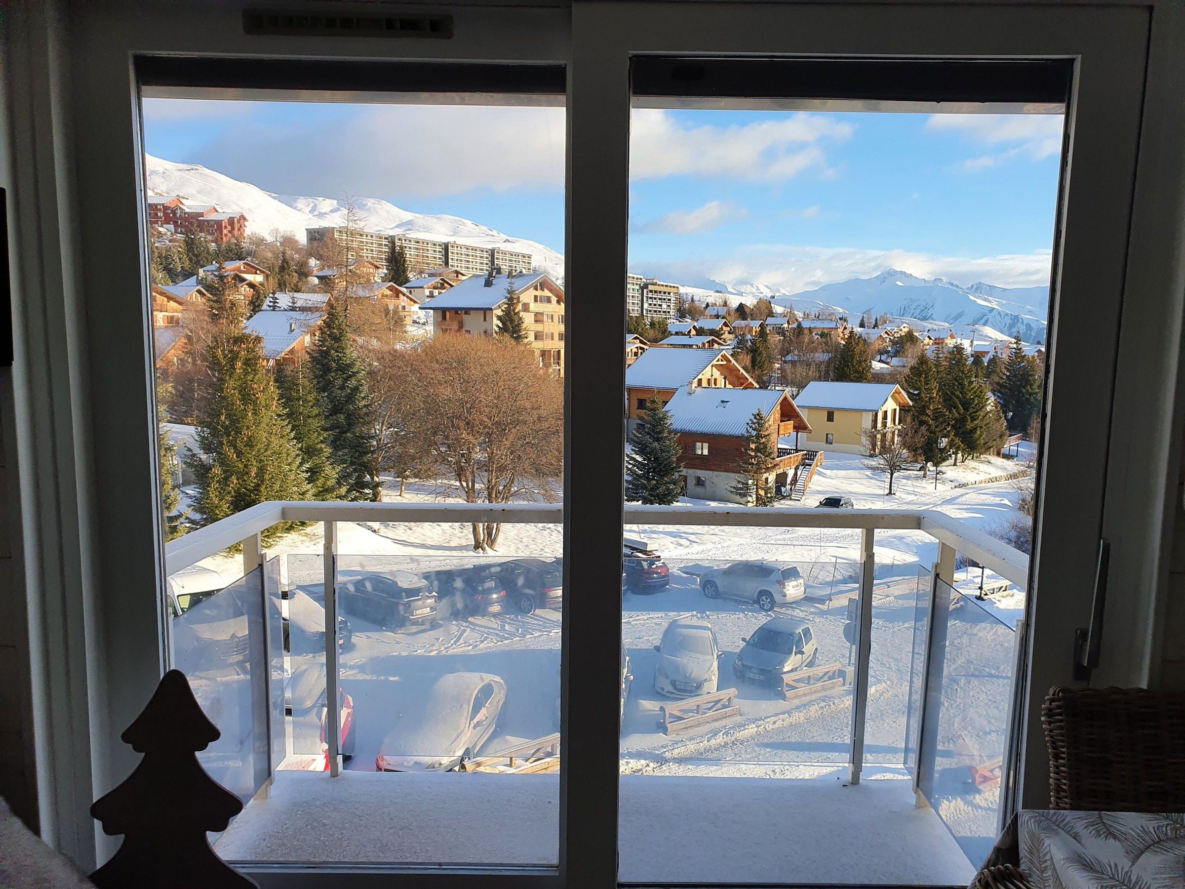 Une vue depuis une fenêtre donnant sur un paysage enneigé, avec des bâtiments et une montagne à l'horizon.