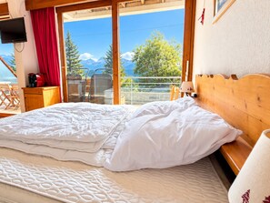 A hotel room with a bed, a TV, a desk with a coffee maker, and a view of trees and mountains. - Apartment mountain view - 5 guests (Chamrousse)