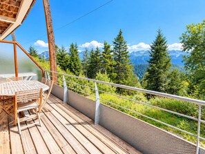 Een houten terras met een tafel en stoelen, met uitzicht op een bebost berglandschap.