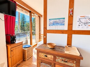 Ein gemütliches Zimmer mit einem Holzschrank, einem Fernseher, einer Karte an der Wand und einem Fenster mit rotem Vorhang.