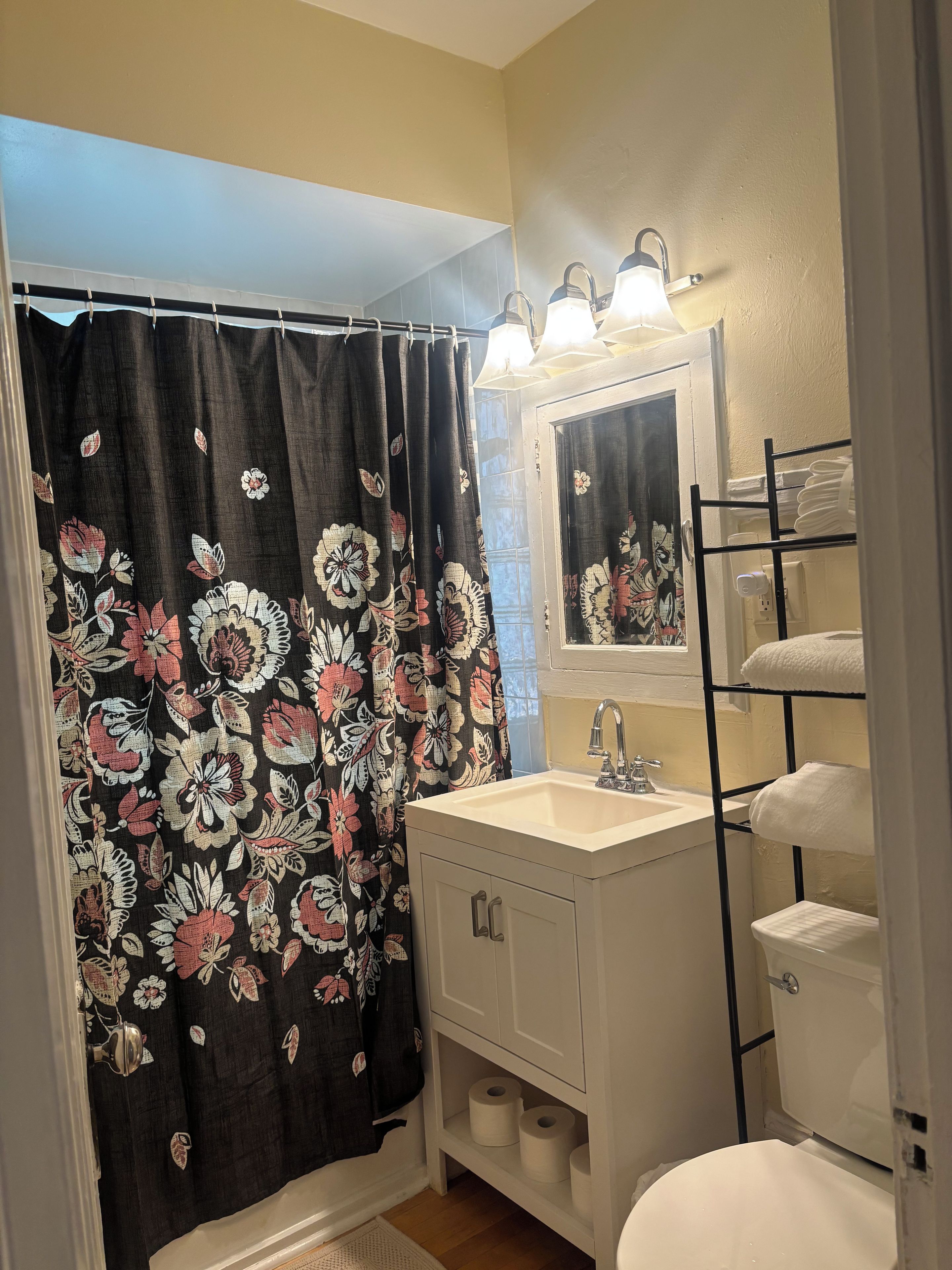 A bathroom with a shower curtain, a sink, a toilet, and a towel rack.