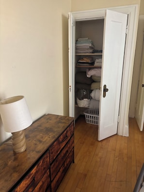 Una habitación con un aparador de madera, una lámpara y una puerta blanca que da a un armario con estantes y una cesta de ropa.