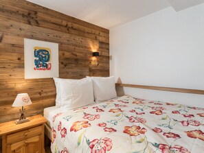 A bedroom with a wooden headboard, a bed with floral bedding, a nightstand with a lamp, and a wall-mounted light fixture. - Luxury apartment, mountain view - 8 guests (Méribel)