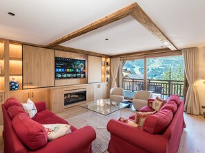 A living room with a fireplace, red sofas, a glass coffee table, and a TV mounted on the wall. - Luxury apartment, mountain view - 8 guests (Méribel)