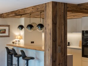A kitchen with a wooden beam ceiling, a bar area with stools, and pendant lights. - Luxury apartment, mountain view - 8 guests (Méribel)