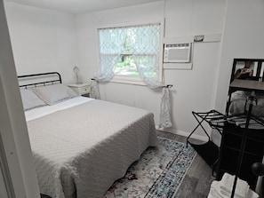 Une chambre à coucher comprenant un lit, une table de chevet, une fenêtre avec des rideaux, un radiateur et un miroir.