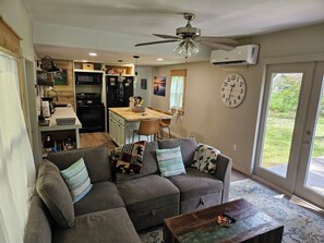 A living room with a grey sofa, a coffee table, and a kitchen area in the background. - Welcome to Gator Bait Getaway! Tucked among the pines near Salt Springs. (Fort McCoy)