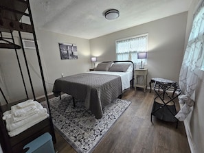 A bedroom with a bed, bedside table, lamp, and a small chair. - Welcome to Gator Bait Getaway! Tucked among the pines near Salt Springs. (Fort McCoy)