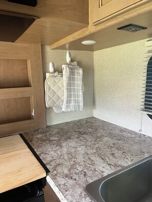 A kitchen with a marble countertop, wooden cabinets, and a built-in sink. - Thor Motor Coach Bunkhouse non stationary. 
Monarch Meadows RV (Greenfield)