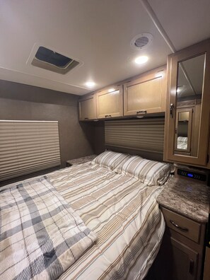 A bedroom with a bed, a nightstand, a dresser, and a mirror. - Thor Motor Coach Bunkhouse non stationary. 
Monarch Meadows RV (Greenfield)