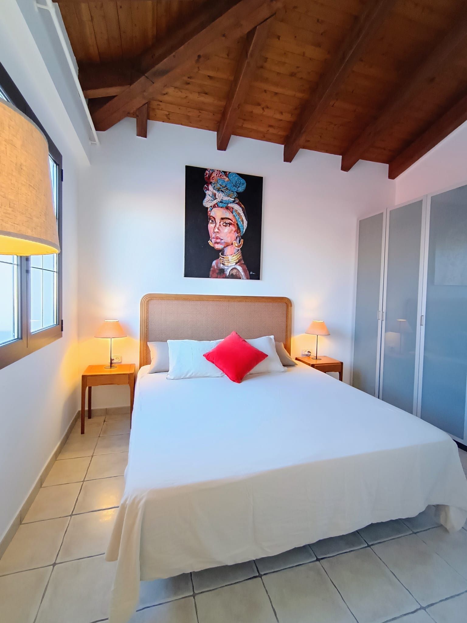 Een slaapkamer met een groot bed, twee bedlampen, een schilderij aan de muur en een kledingkast.