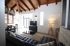 Uma sala de estar com um sofá de couro preto, uma televisão e um espaço de jantar com mesa e cadeiras.