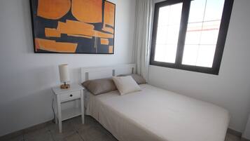 Une chambre à coucher avec un lit, une table de chevet, une lampe, une fenêtre et un tableau au mur.