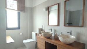 Et moderne badeværelse med en trækommode, to store spejle, et toilet og et vindue med skodder.