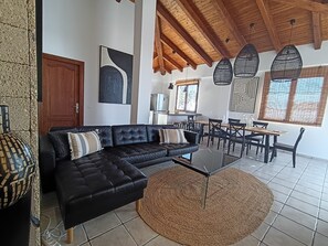 Un saló modern amb un sofà de pell negra, una taula de centre rodona i una zona de menjador amb taula i cadires de fusta.