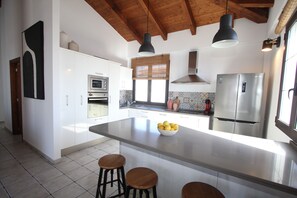 A modern kitchen with white cabinets, stainless steel appliances, a large island with stools, and pendant lighting.