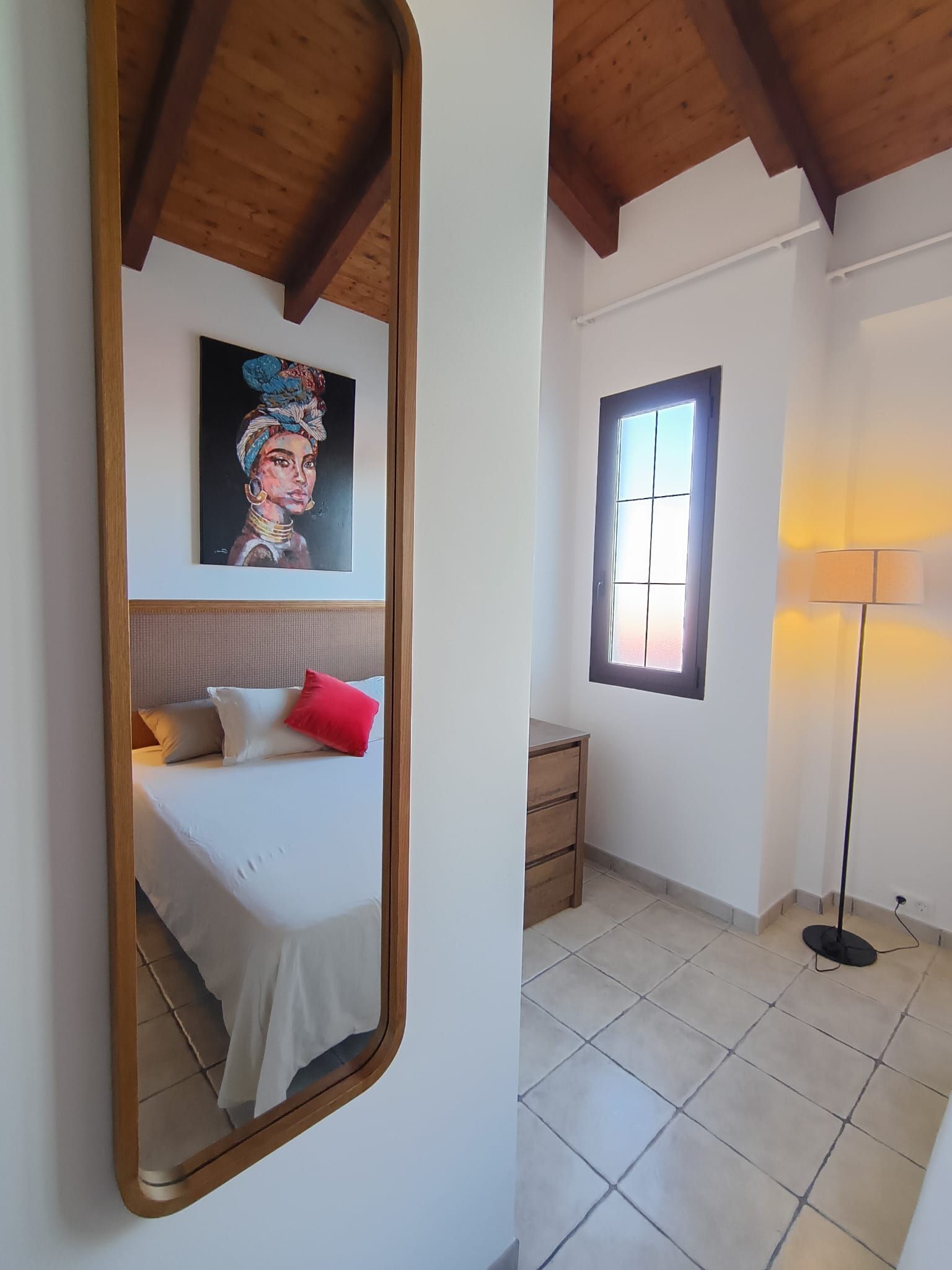 Ein Schlafzimmer mit Bett, Nachttisch, Lampe, Fenster und einem Bild an der Wand.