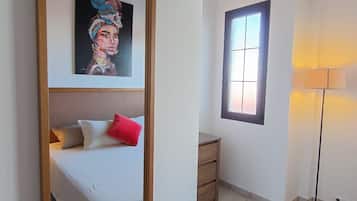 Ein Schlafzimmer mit Bett, Nachttisch, Lampe, Fenster und einem Bild an der Wand.