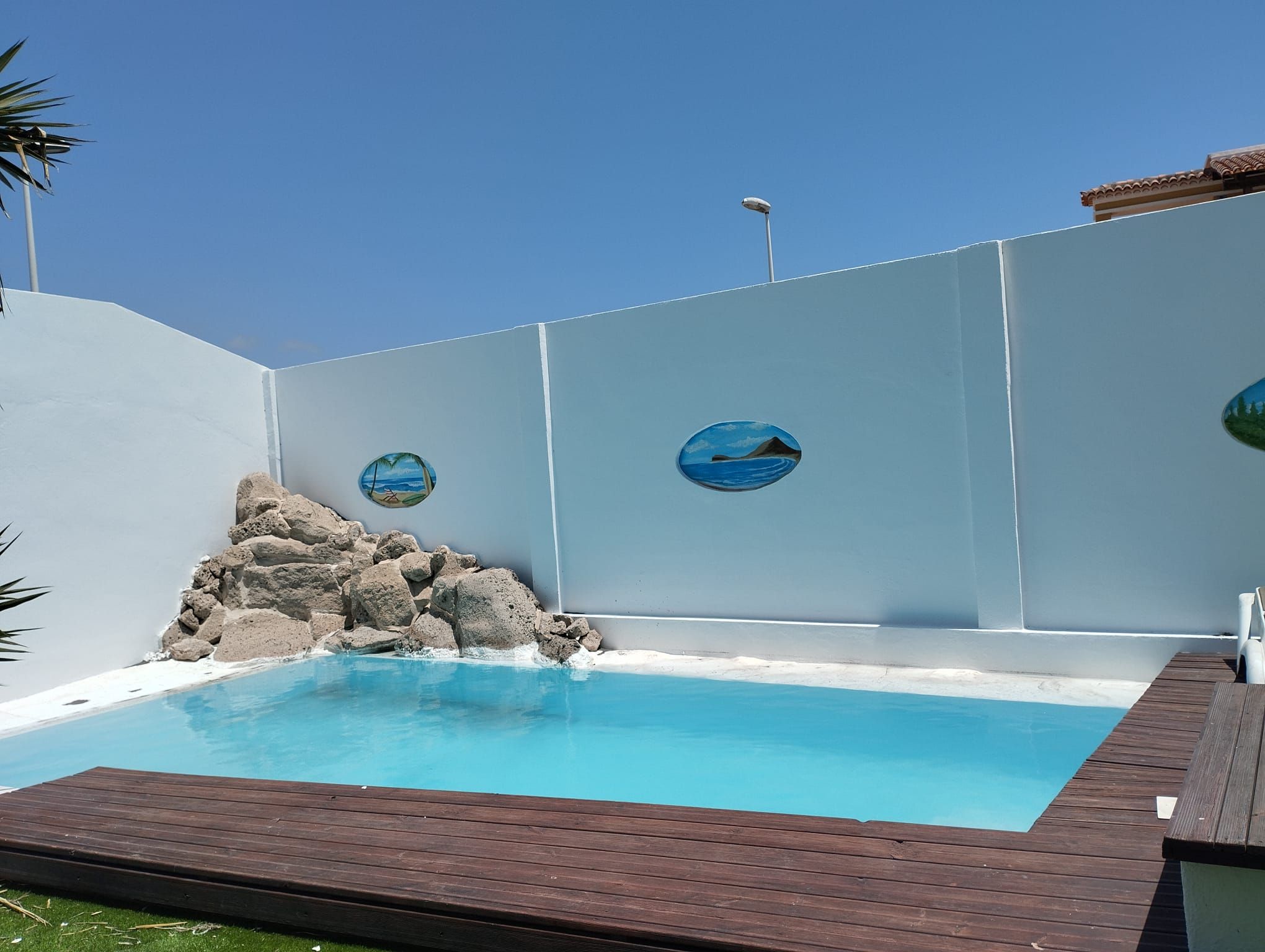 Una piscina amb un pont de fusta, una formació rocosa i dues decoracions circulars a la paret.