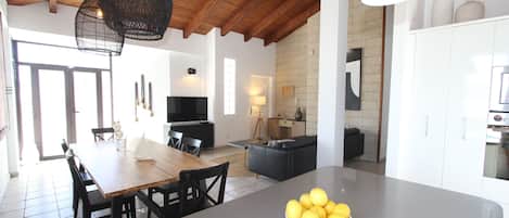Una cocina moderna con una isla central, una zona de comedor con mesa y sillas de madera, y un espacio de sala de estar con sofá y televisor.
