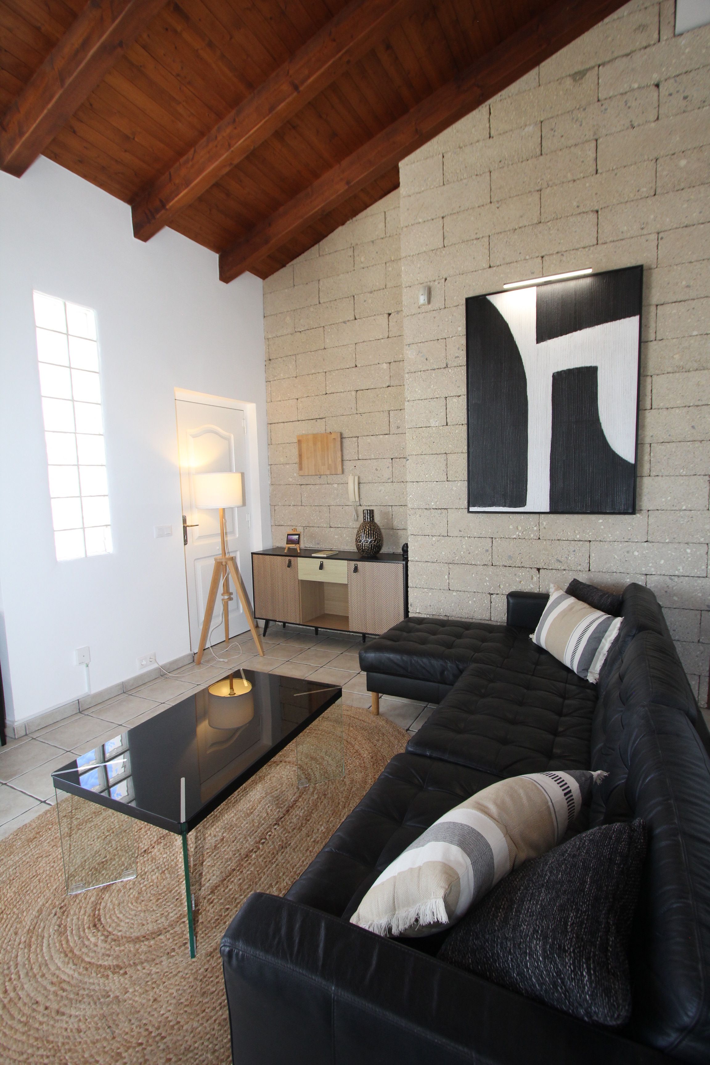 Een woonkamer met een zwarte leren bank, een houten salontafel, een lamp en een groot abstract schilderij aan de muur.